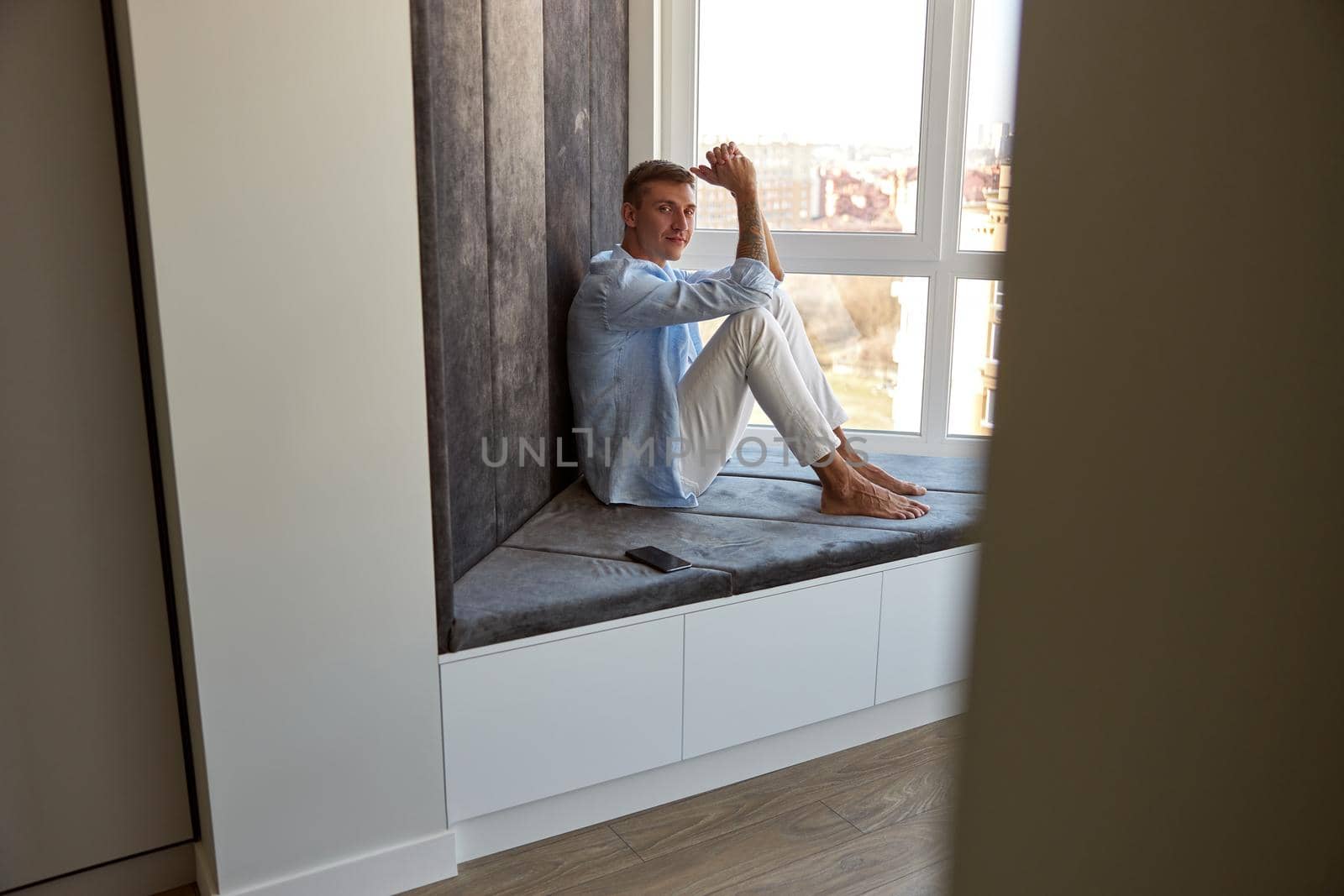 Happy adult caucasian male is sitting near panoramic window and chilling