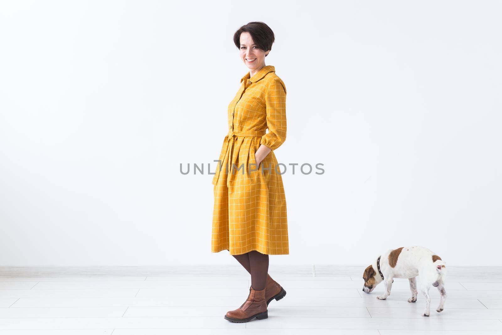 Cheerful young woman posing in a yellow dress with her beloved dog Jack Russell Terrier standing on a white background. The concept of casual wear