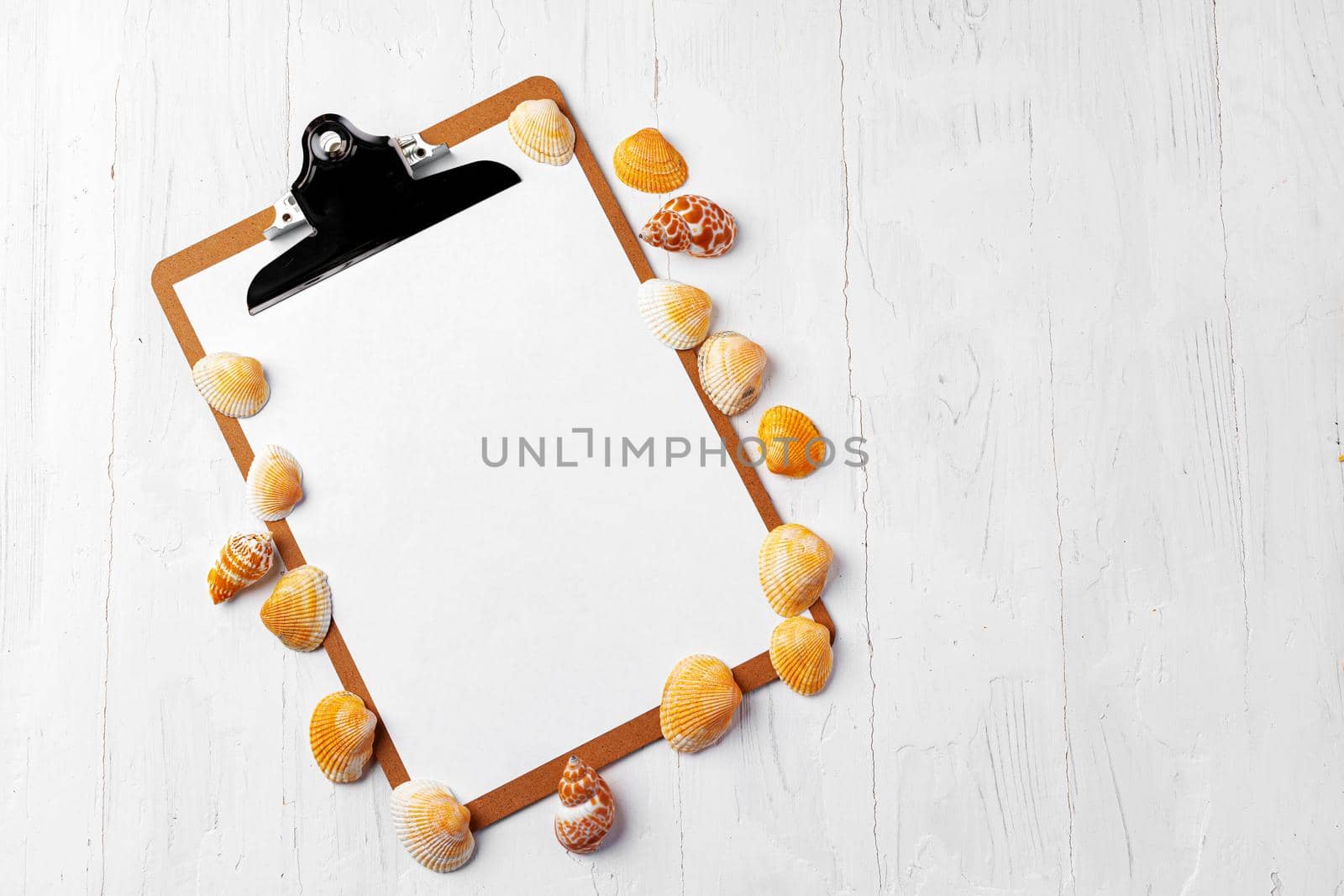 Clipboard with sea shells on white wooden table close up, copy space.