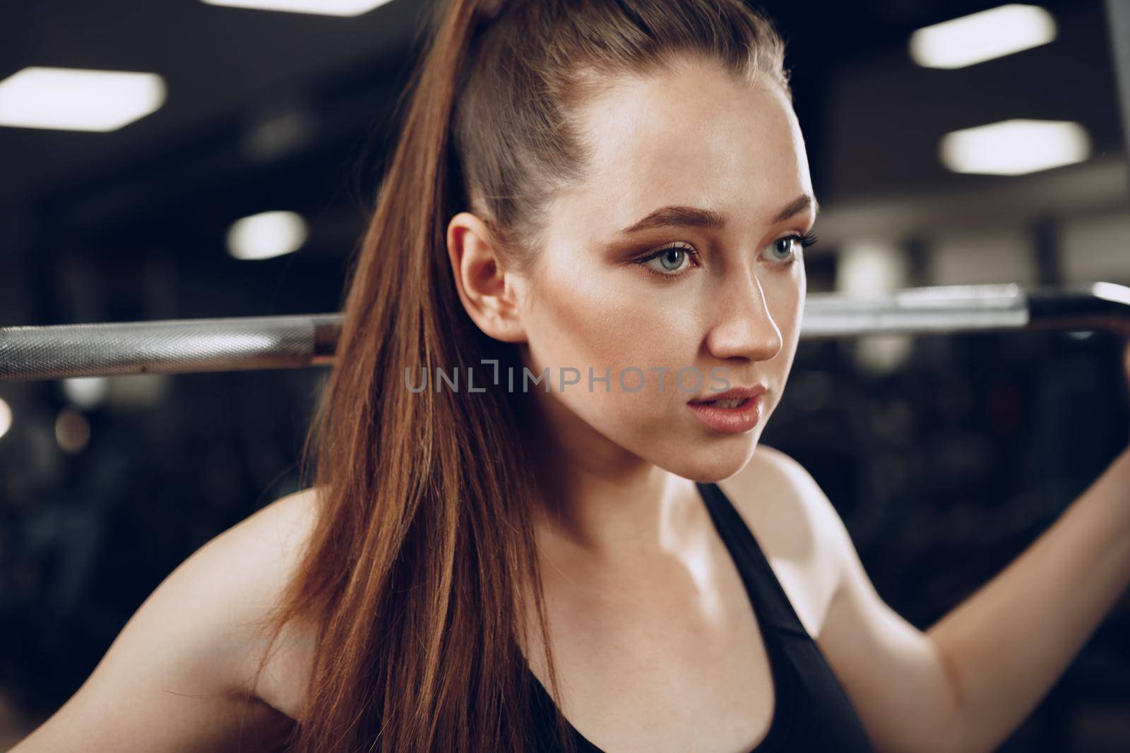 Attractive young woman doing exercises for the muscles of the arms and back in a gym close up