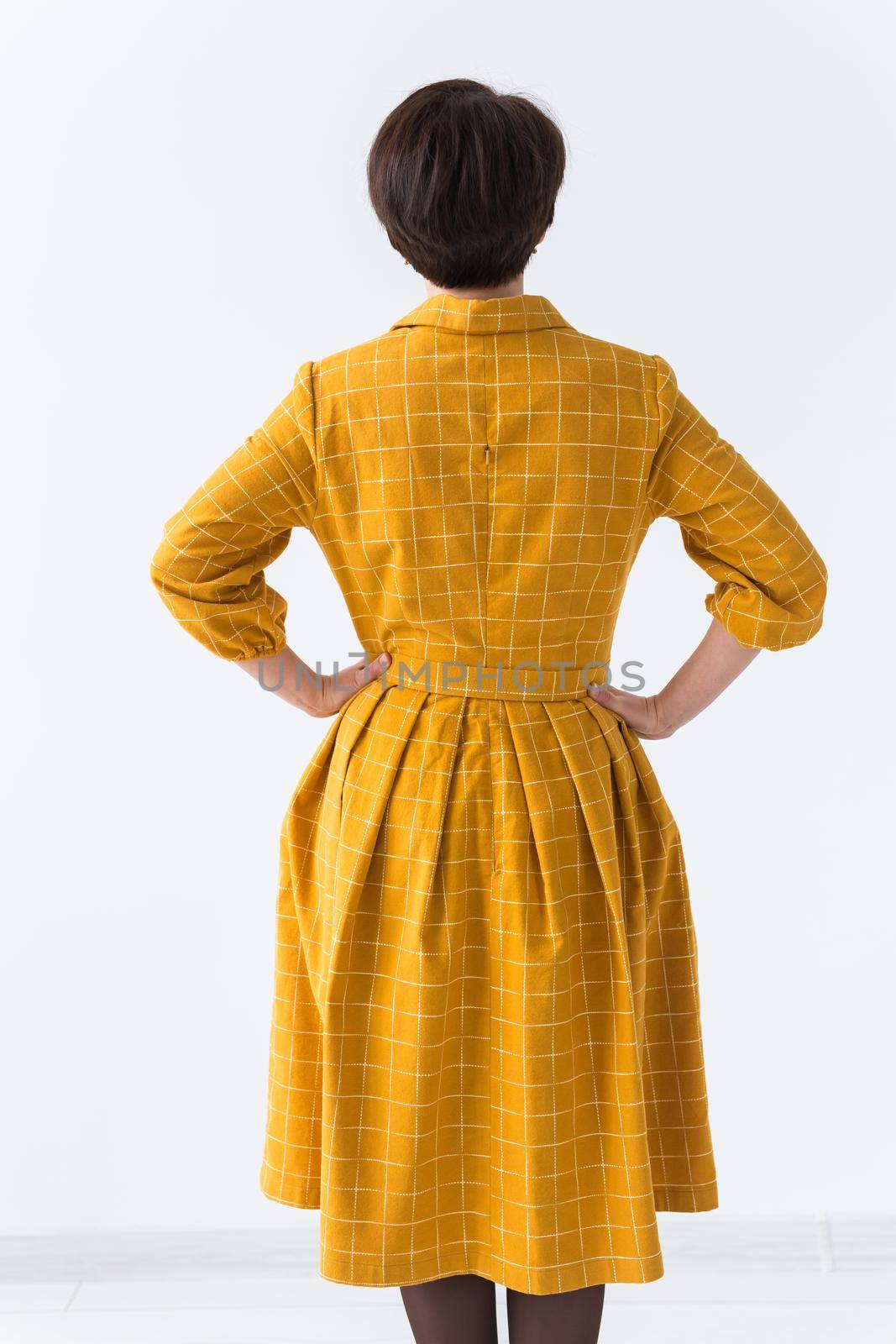 clothing, designer, people concept - back view of attractive woman in a yellow dress posing on white room