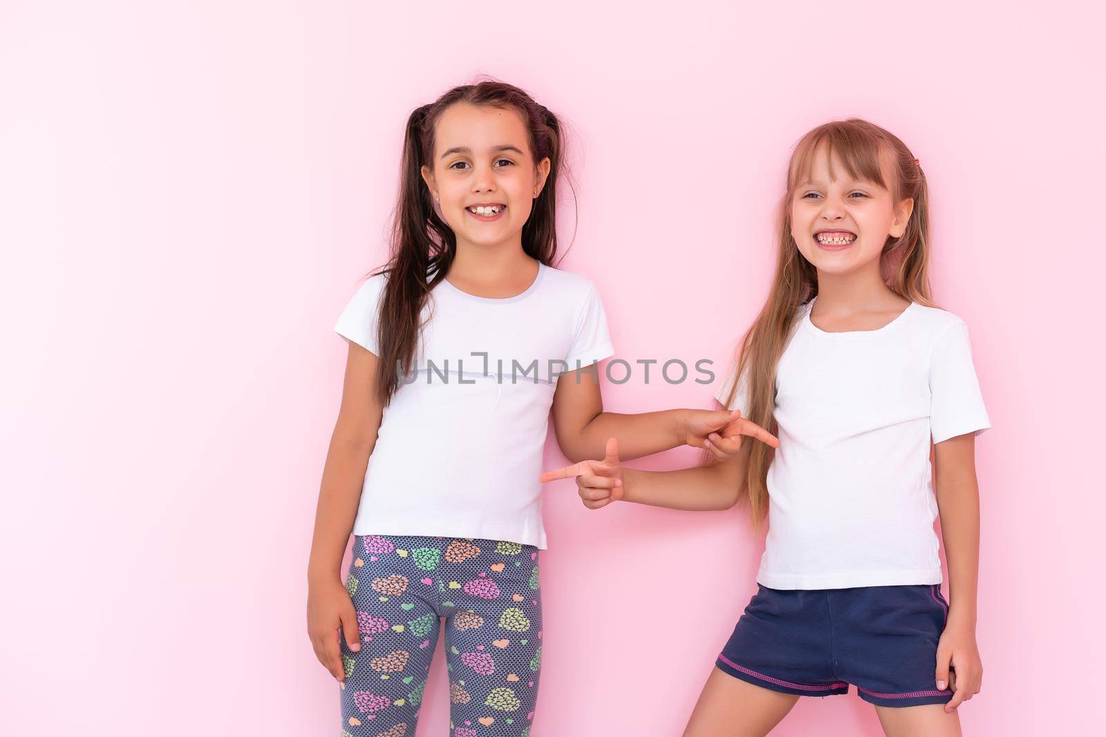 Two little girls - best friends, isolated over on a pink background by Andelov13