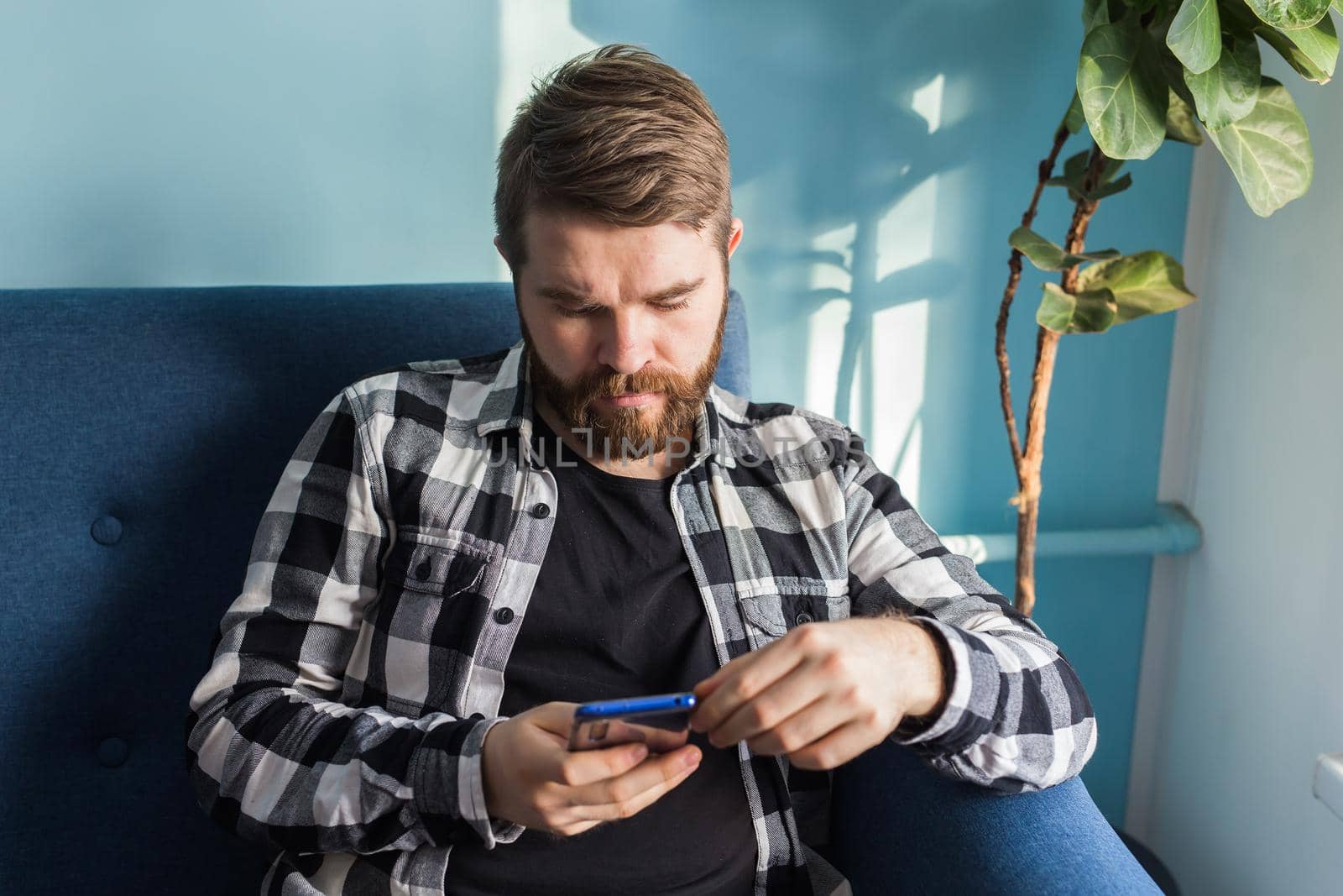 Technologies and leisure concept - Cheerful man sitting on the couch using his smartphone at home in living room.