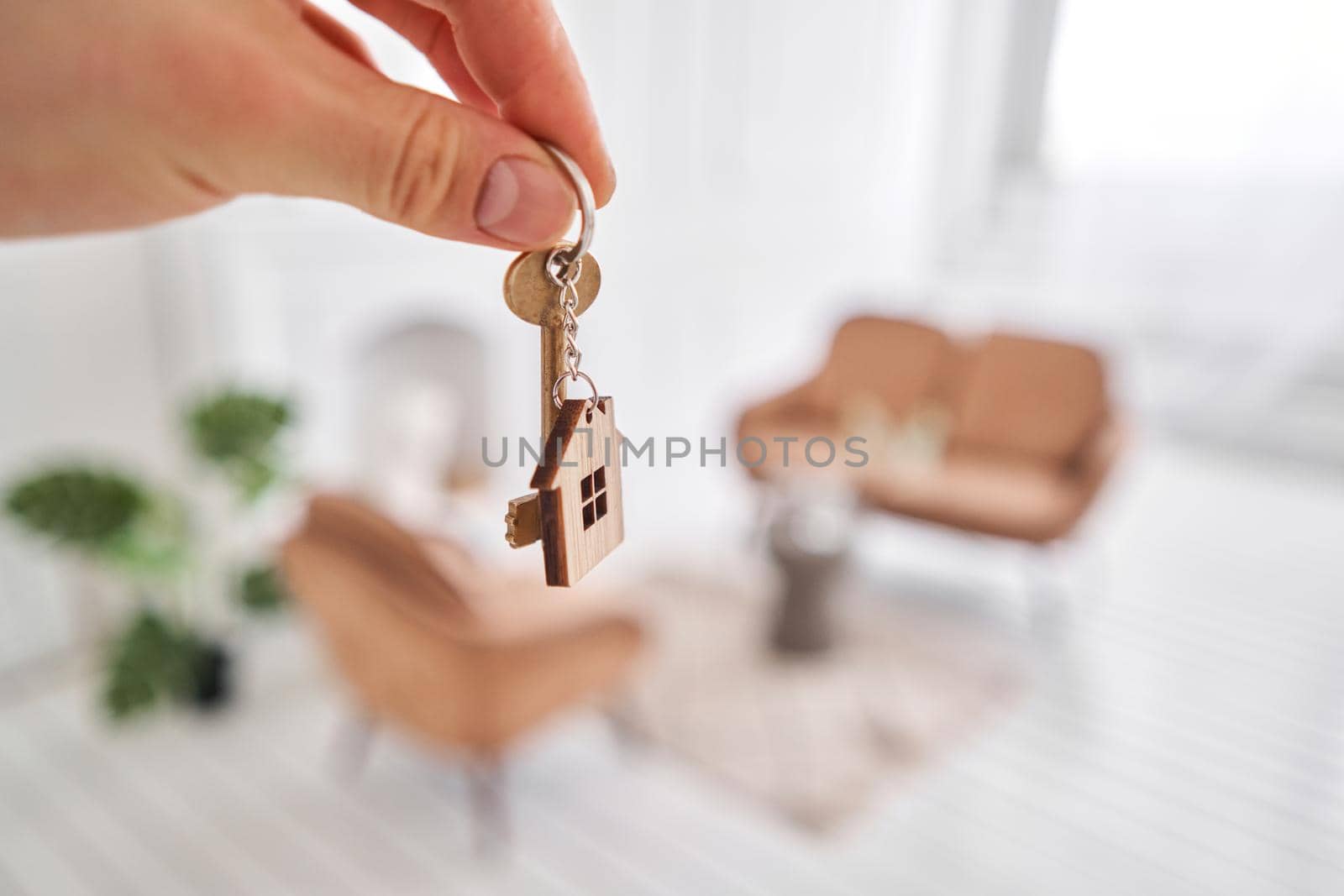 Men hand holding key with house shaped keychain. Modern light lobby interior. Mortgage concept. Real estate, moving home or renting property