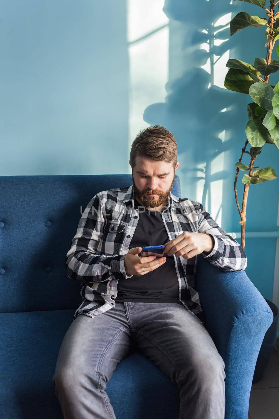 Technologies and leisure concept - Handsome man using smartphone sitting at home