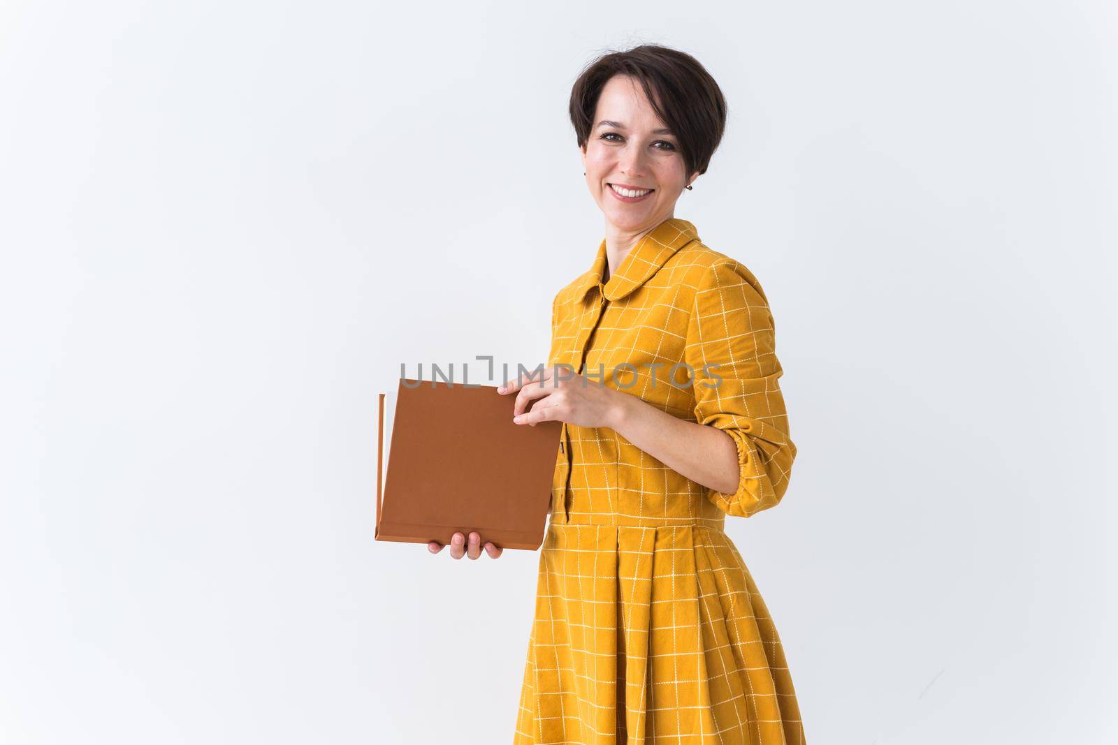Portrait of a beautiful brunette girl in a yellow retro dress reading a book on white background.