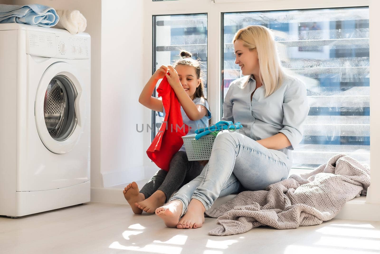 Young housewife and little girl doing laundry together