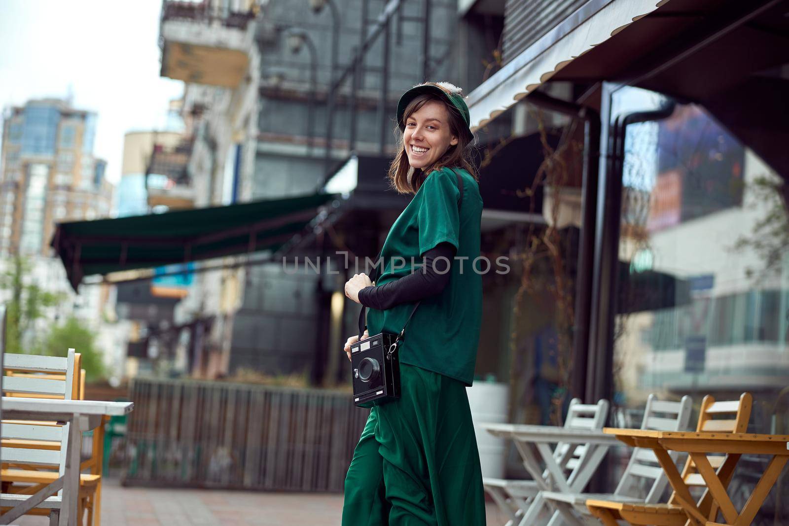 Happy young caucasian lady in green dress is walking near cozy cafe