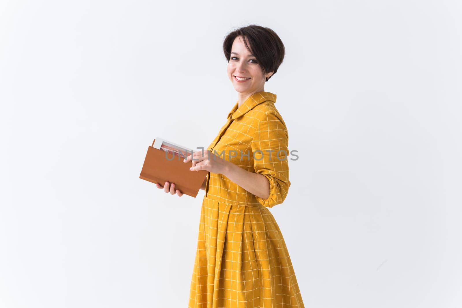 Portrait of a beautiful brunette girl in a yellow retro dress reading a book on white background.