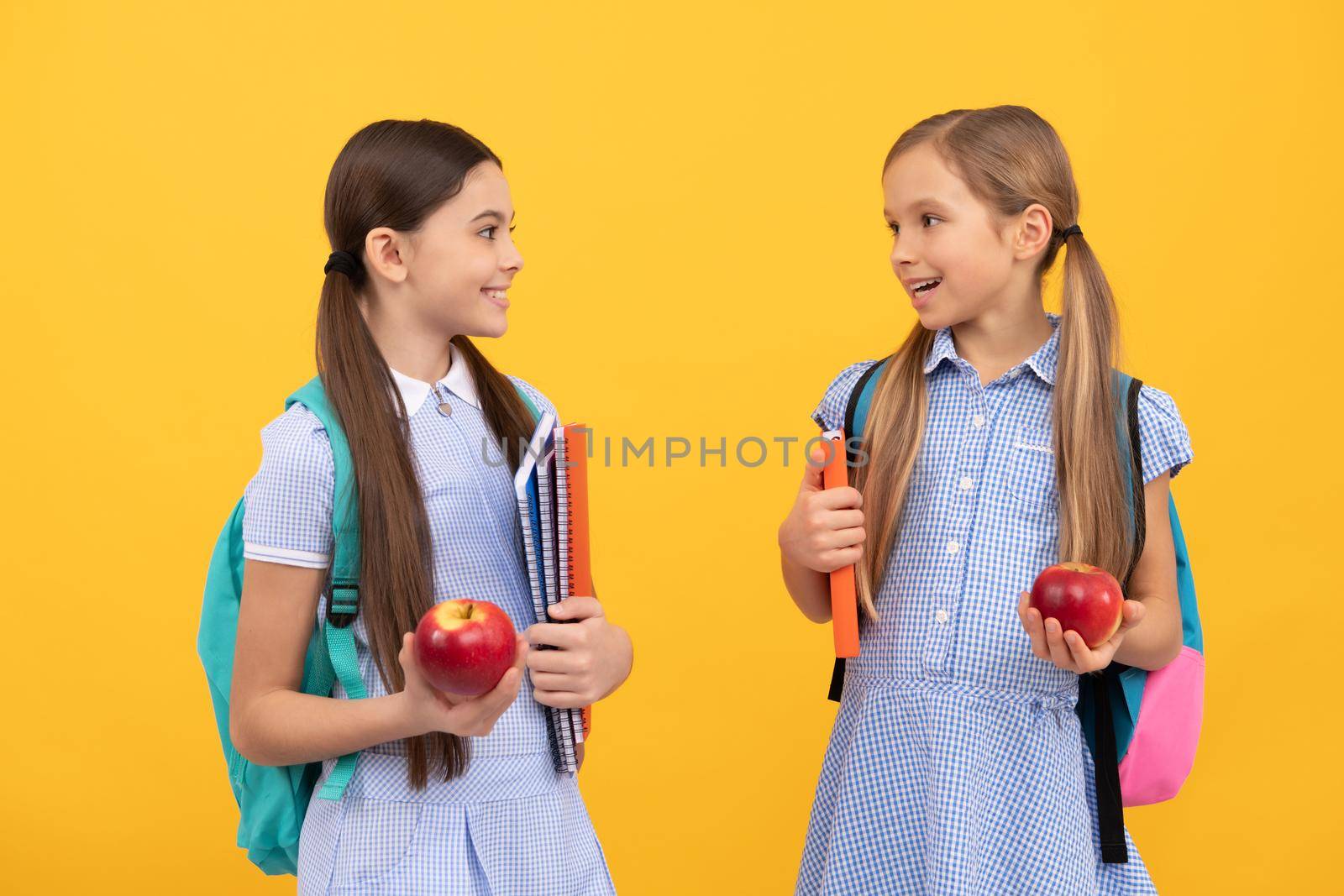 Happy children friends back to school holding books and apples for healthy diet yellow background, dieting.