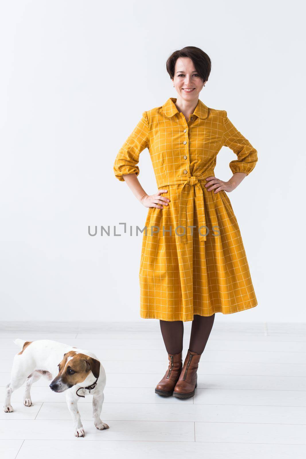 Cheerful young woman posing in a yellow dress with her beloved dog Jack Russell Terrier standing on a white background. The concept of casual wear and pets by Satura86