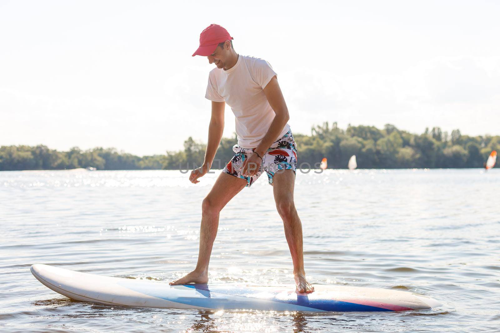 Portrait of a surfer with a SUP Board on the beach. Young man on paddleboard at dawn. The concept of extreme sports. Male surfer lifestyle.