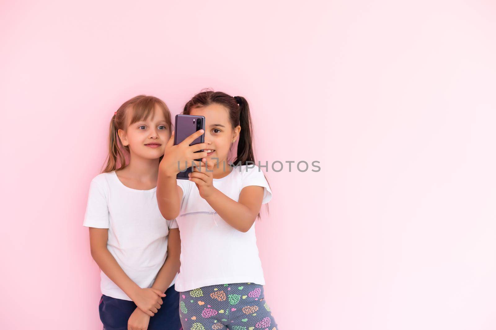 two little girls with a smartphone on a pink background by Andelov13