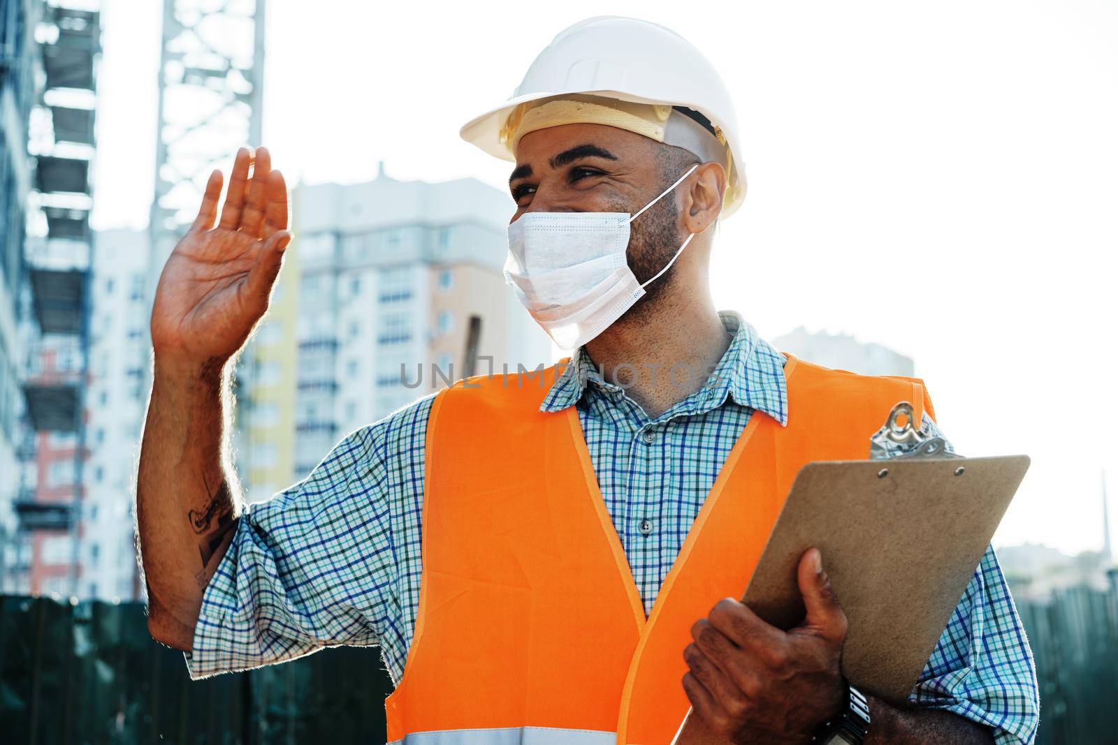 Portrait of mixed race man builder in workwear and hardhat wearing medical mask, close up photo