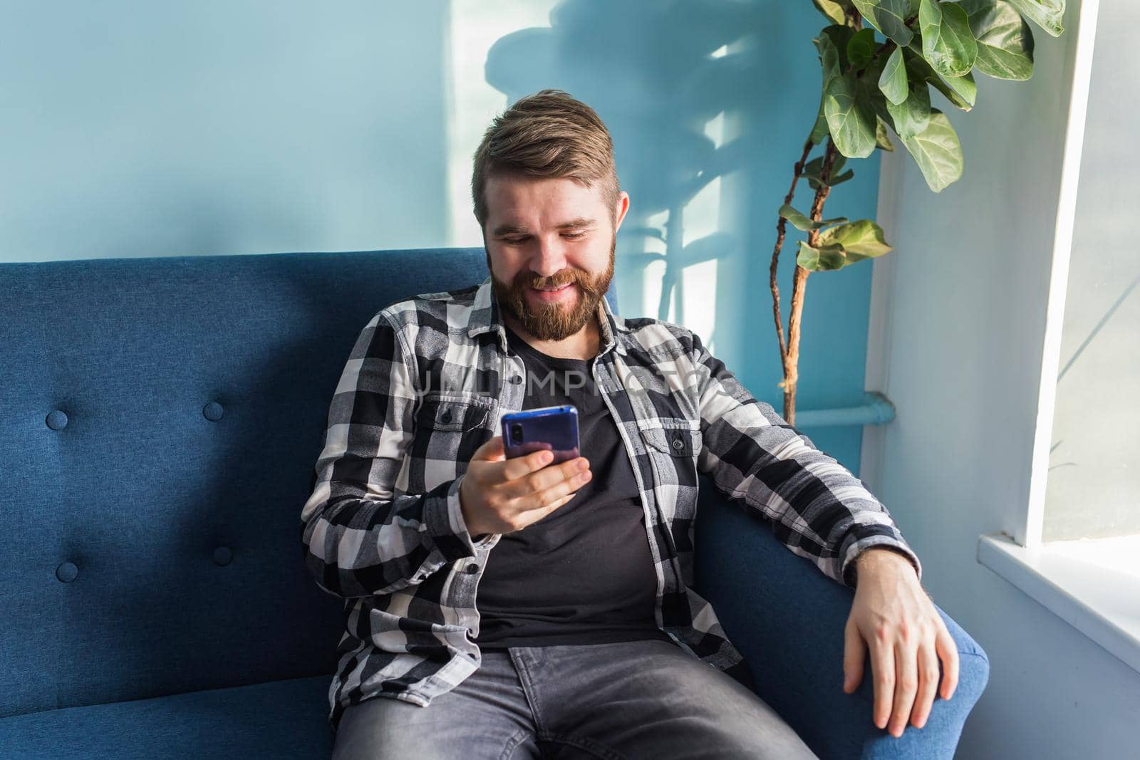 Technologies and leisure concept - Cheerful man sitting on the couch using his smartphone at home in living room.