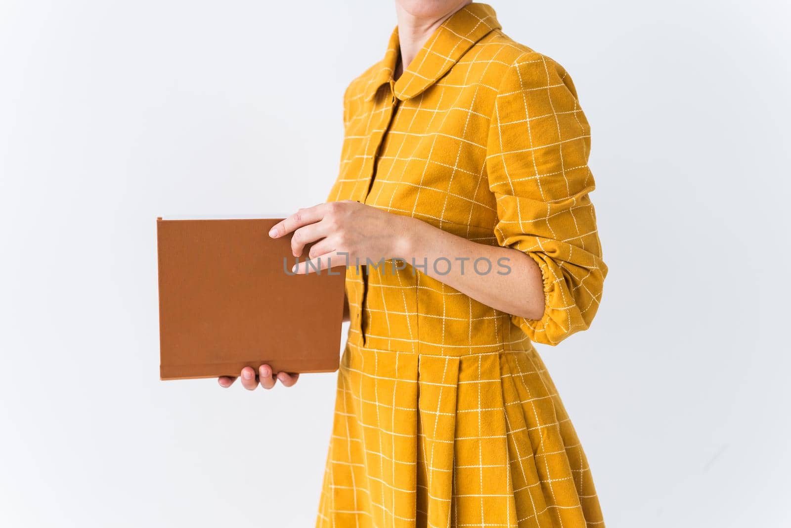 Portrait of a beautiful brunette girl in a yellow retro dress reading a book on white background.