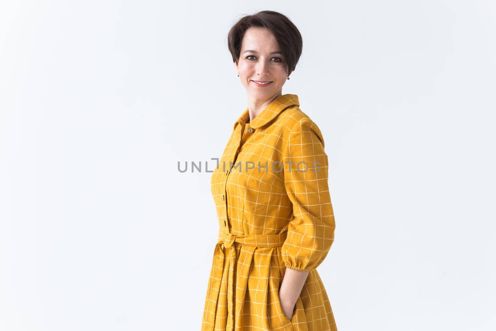 Portrait of a happy young woman in bright yellow dress over white room background. Beauty, fashion concept