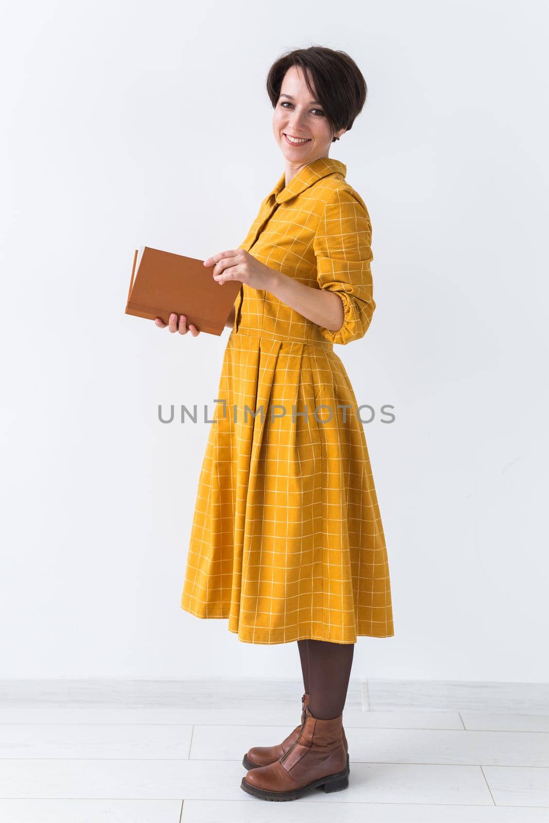 Portrait of a beautiful brunette girl in a yellow retro dress reading a book on white background.