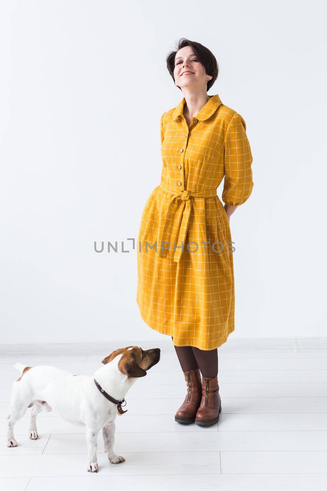 Cheerful young woman posing in a yellow dress with her beloved dog Jack Russell Terrier standing on a white background. The concept of casual wear