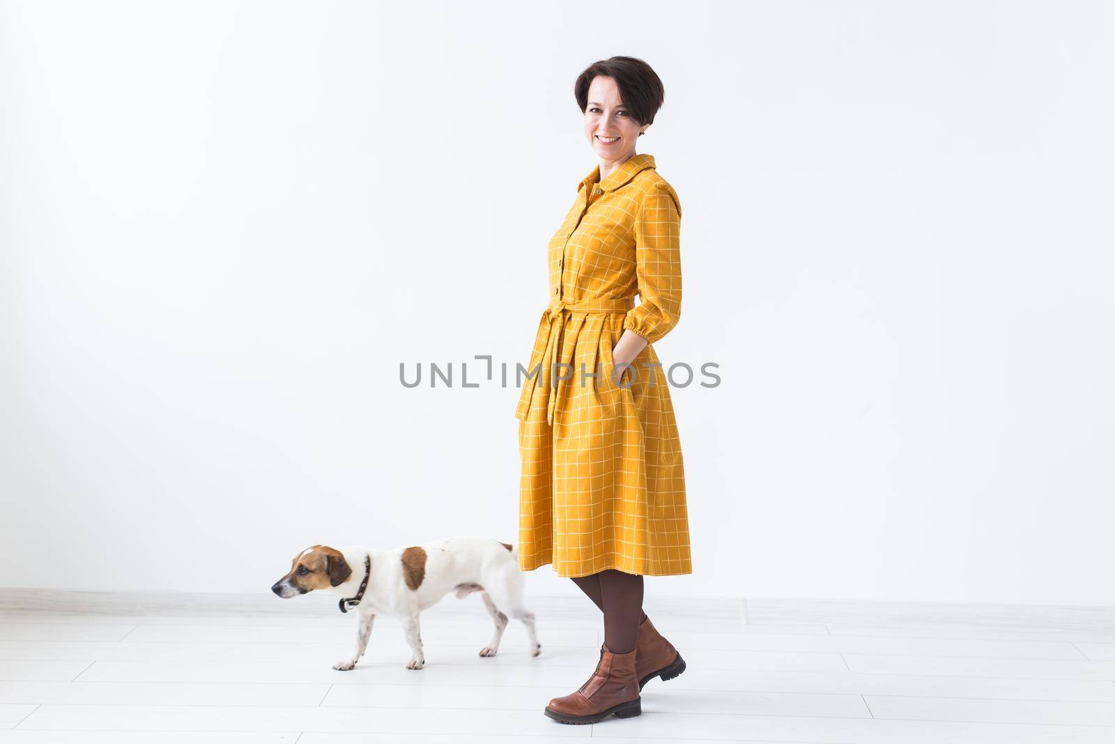 Cheerful young woman posing in a yellow dress with her beloved dog Jack Russell Terrier standing on a white background. The concept of casual wear