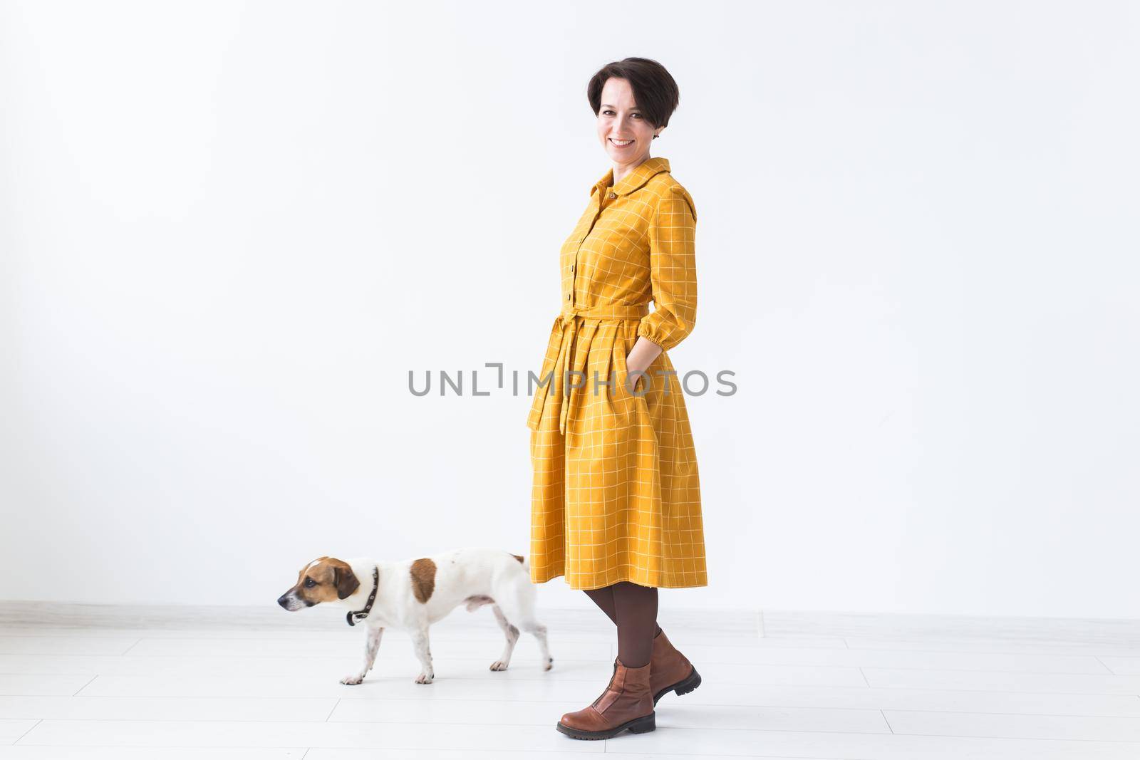 Cheerful young woman posing in a yellow dress with her beloved dog Jack Russell Terrier standing on a white background. The concept of casual wear and pets by Satura86