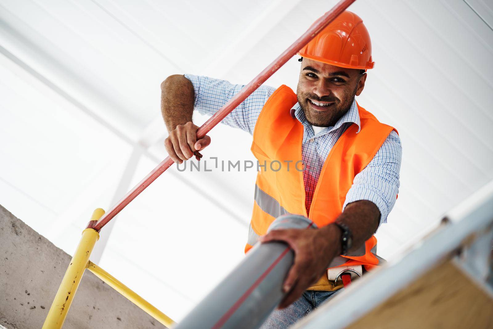 Young handsome builder climbing on scaffolding at construction site, close up