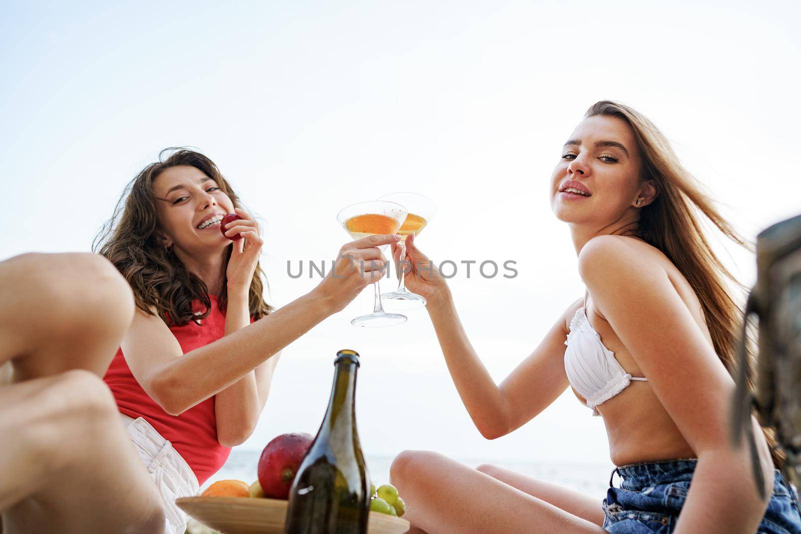 Two young female friends having a picnic on a beach drinking cocktails