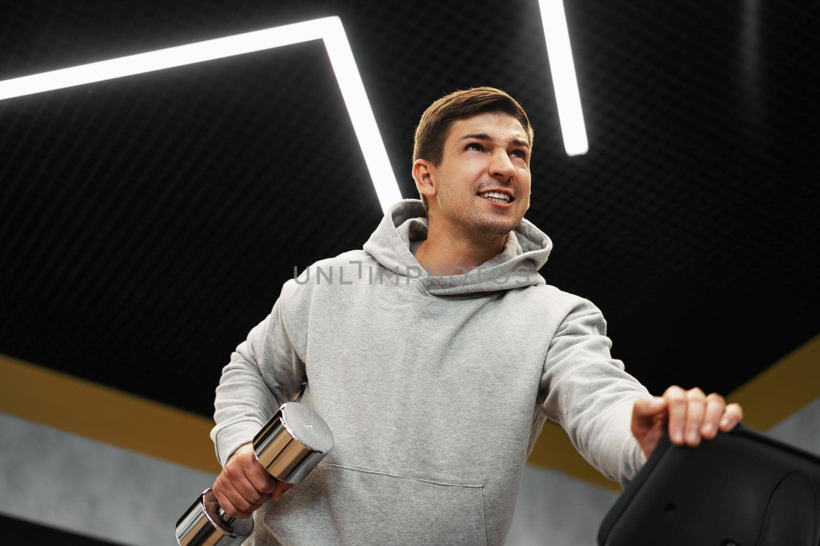 Determined handsome young male working out in gym with dumbbells, close up