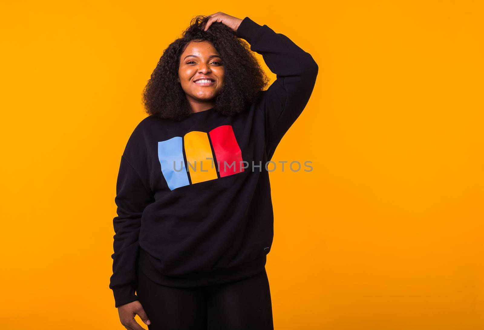 Youth fashion concept - Confident sexy black woman in stylish hoodie having fun on yellow background