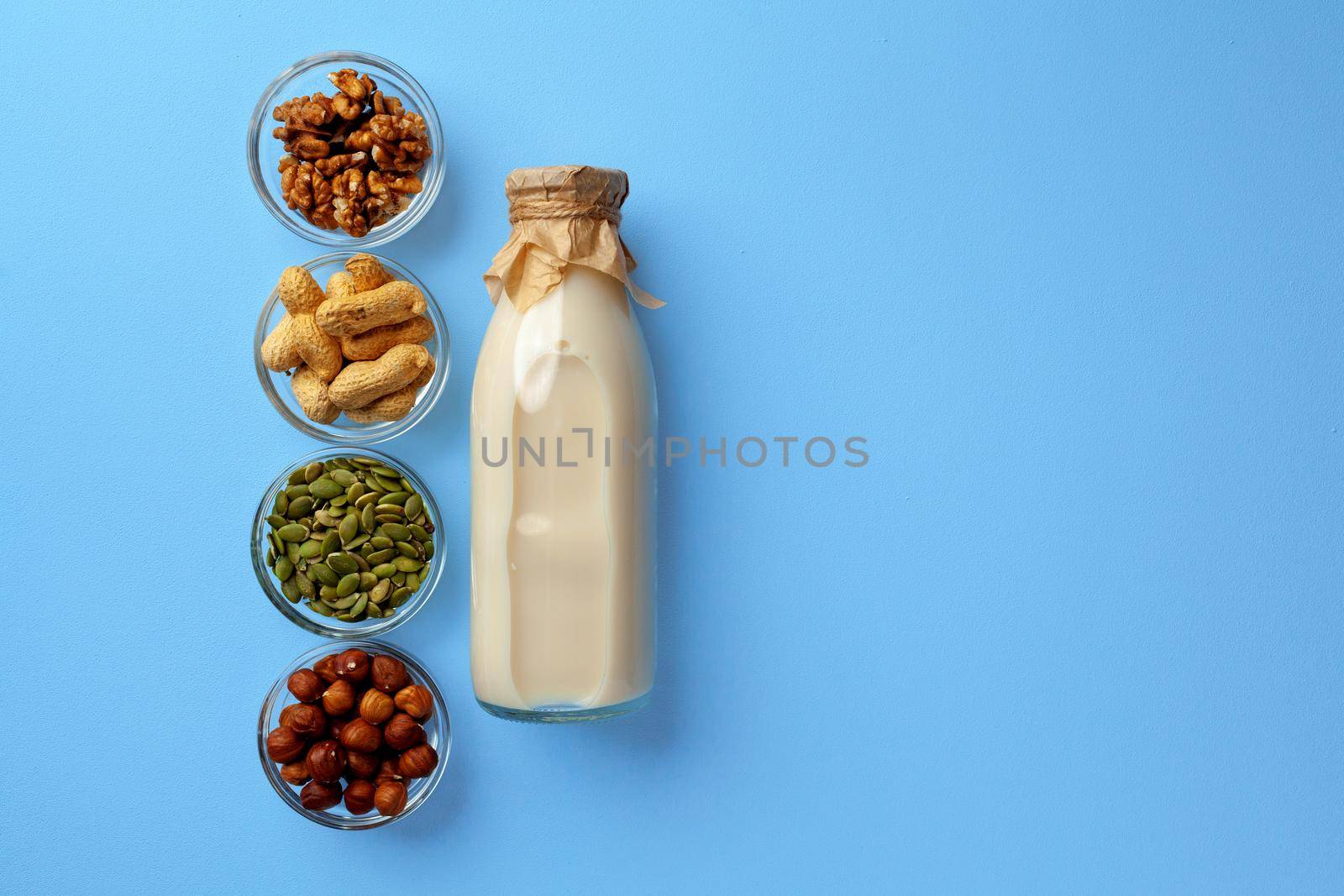 Vegetable milk concept with milk bottle and bowls with grains and nuts on blue background top view