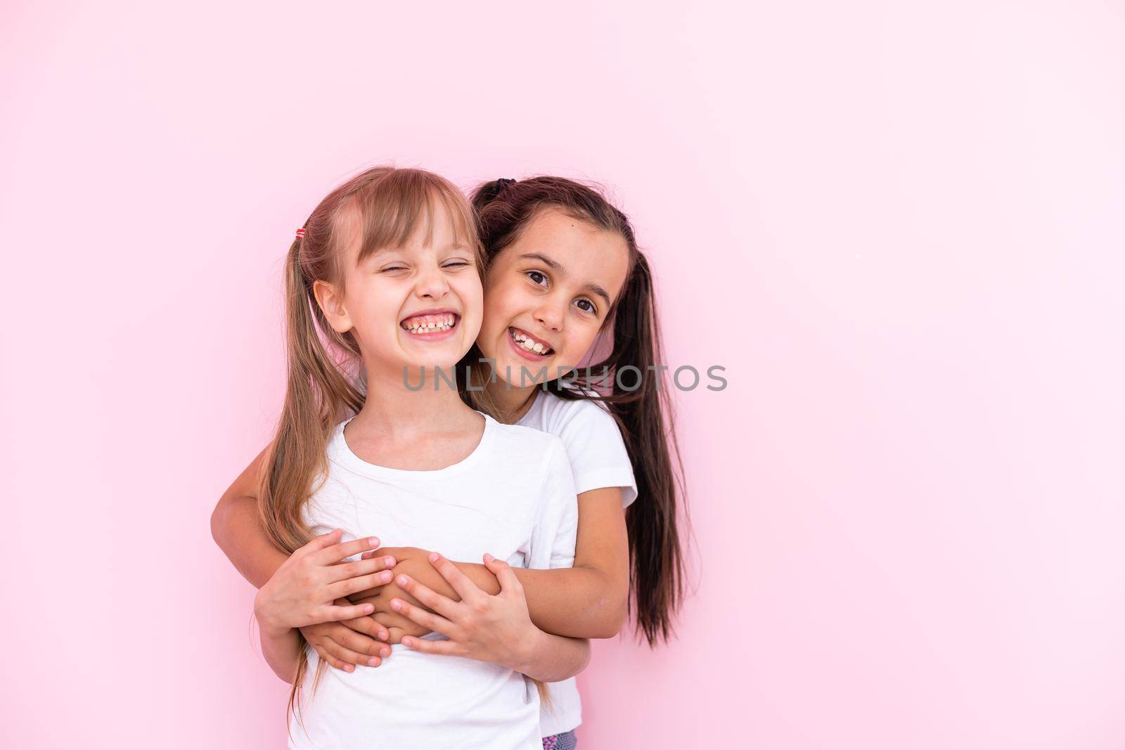 Two little girls - best friends, isolated over on a pink background by Andelov13