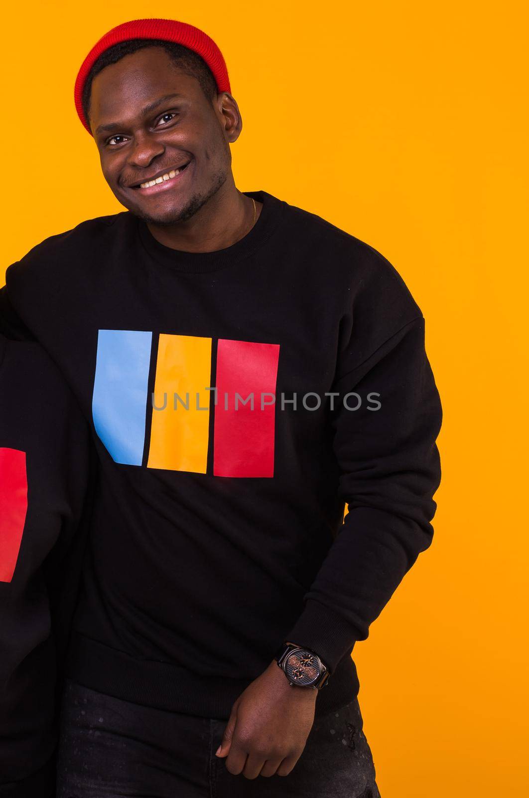 Handsome African American man posing in black sweatshirt on a yellow background. Youth street fashion photo with afro hairstyle. by Satura86