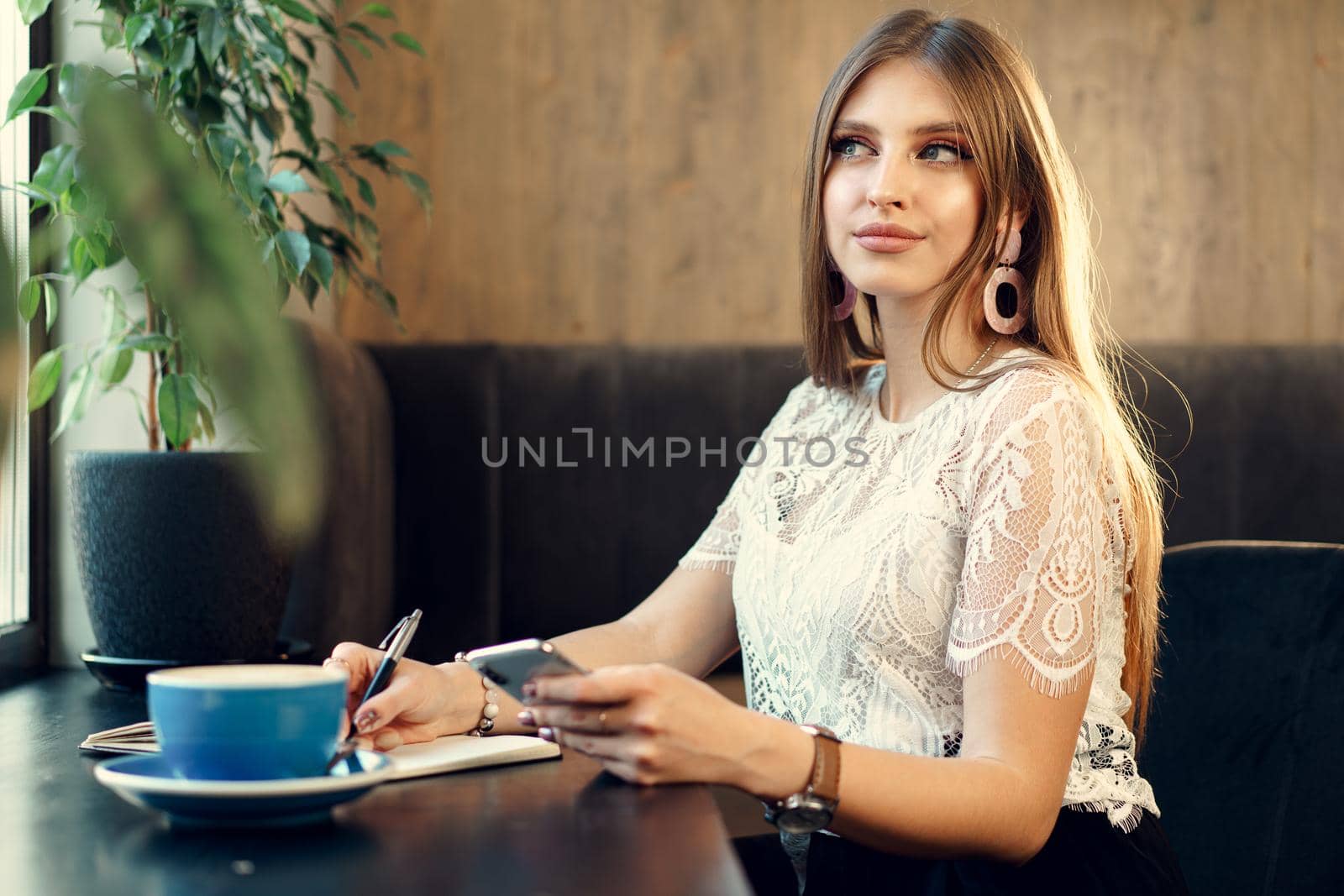 Young business woman sitting at the table in a coffee shop and making notes. Close up.