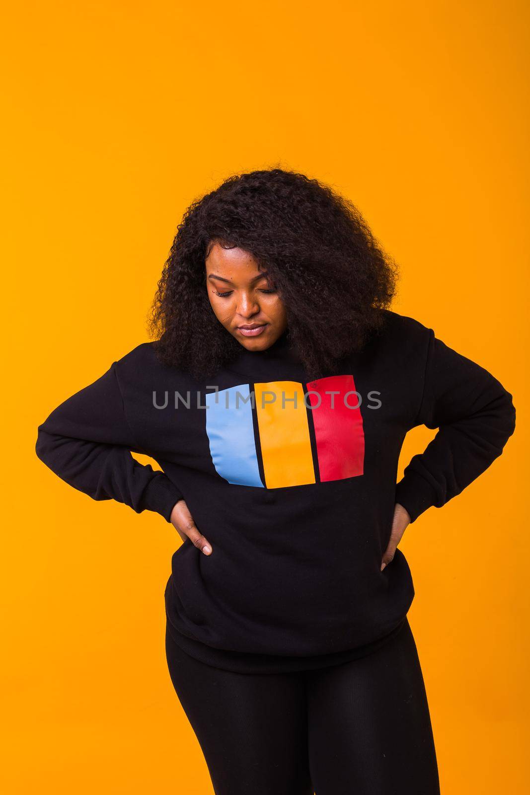 Beautiful African American woman posing in black hoodie on a yellow background. Fashion with afro hairstyle.