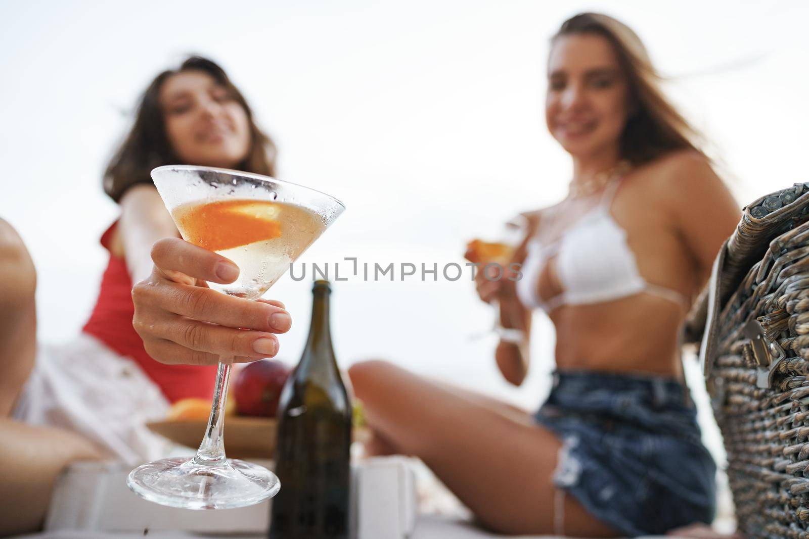 Two young female friends having a picnic on a beach drinking cocktails