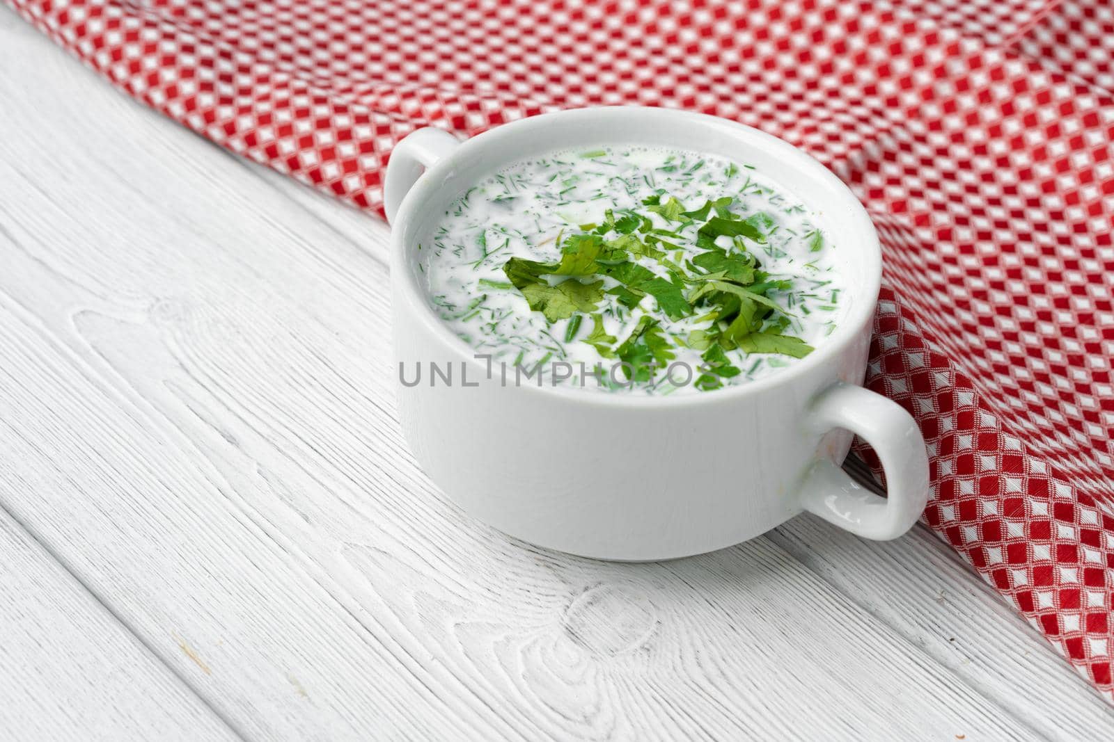 Russian summer cold soup Okroshka on white wooden table with napkin
