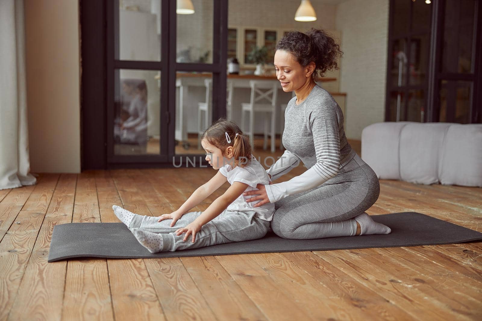 Smiling woman helping daughter with gymnastics at home by Yaroslav_astakhov
