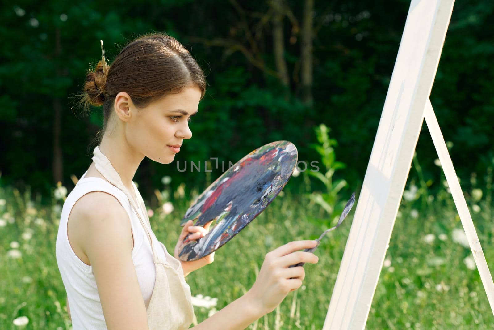 woman artist outdoors with palette of paints paints a picture. High quality photo