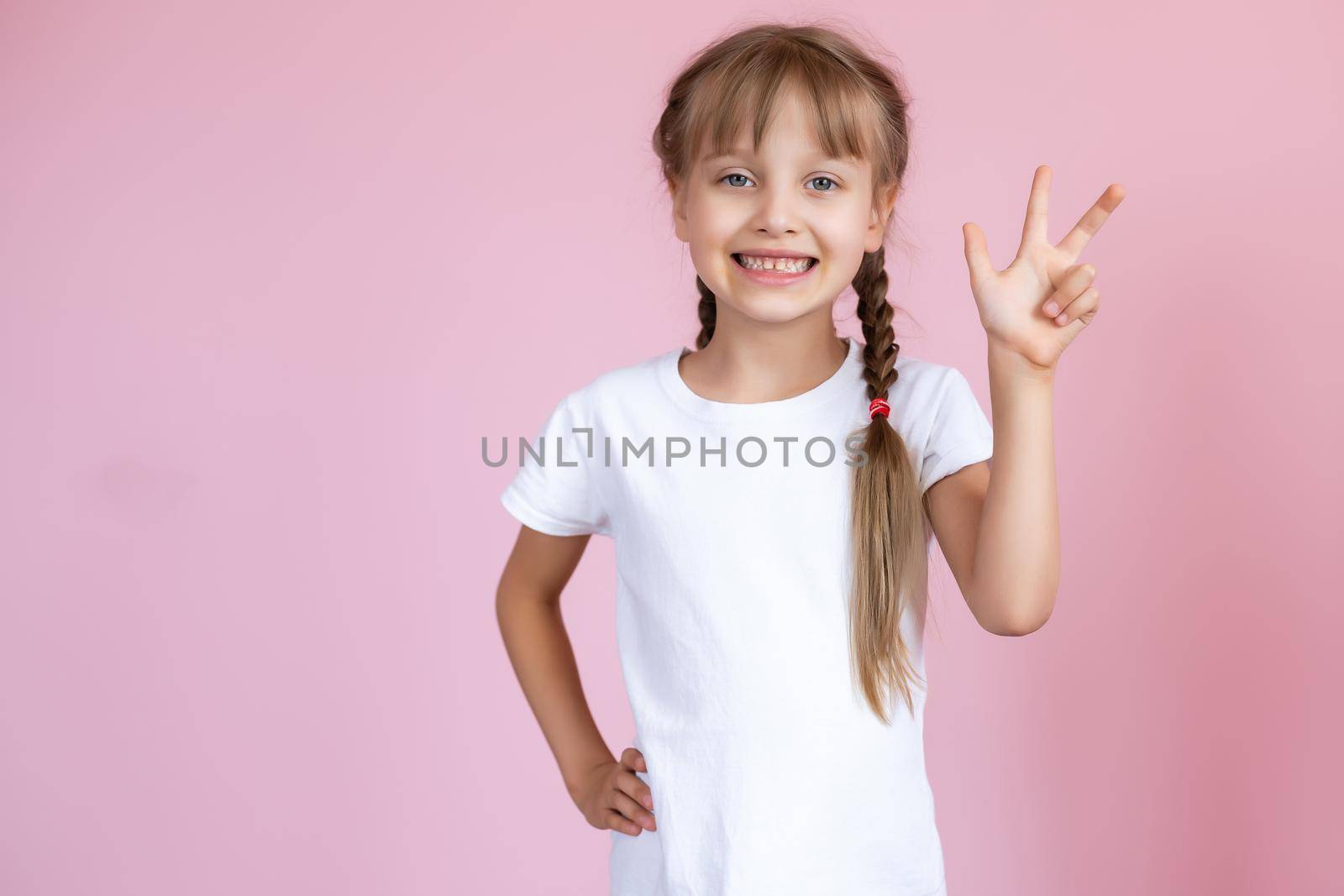 Beautiful little blonde girl with long hair in white T-shirt smiling on a pink background