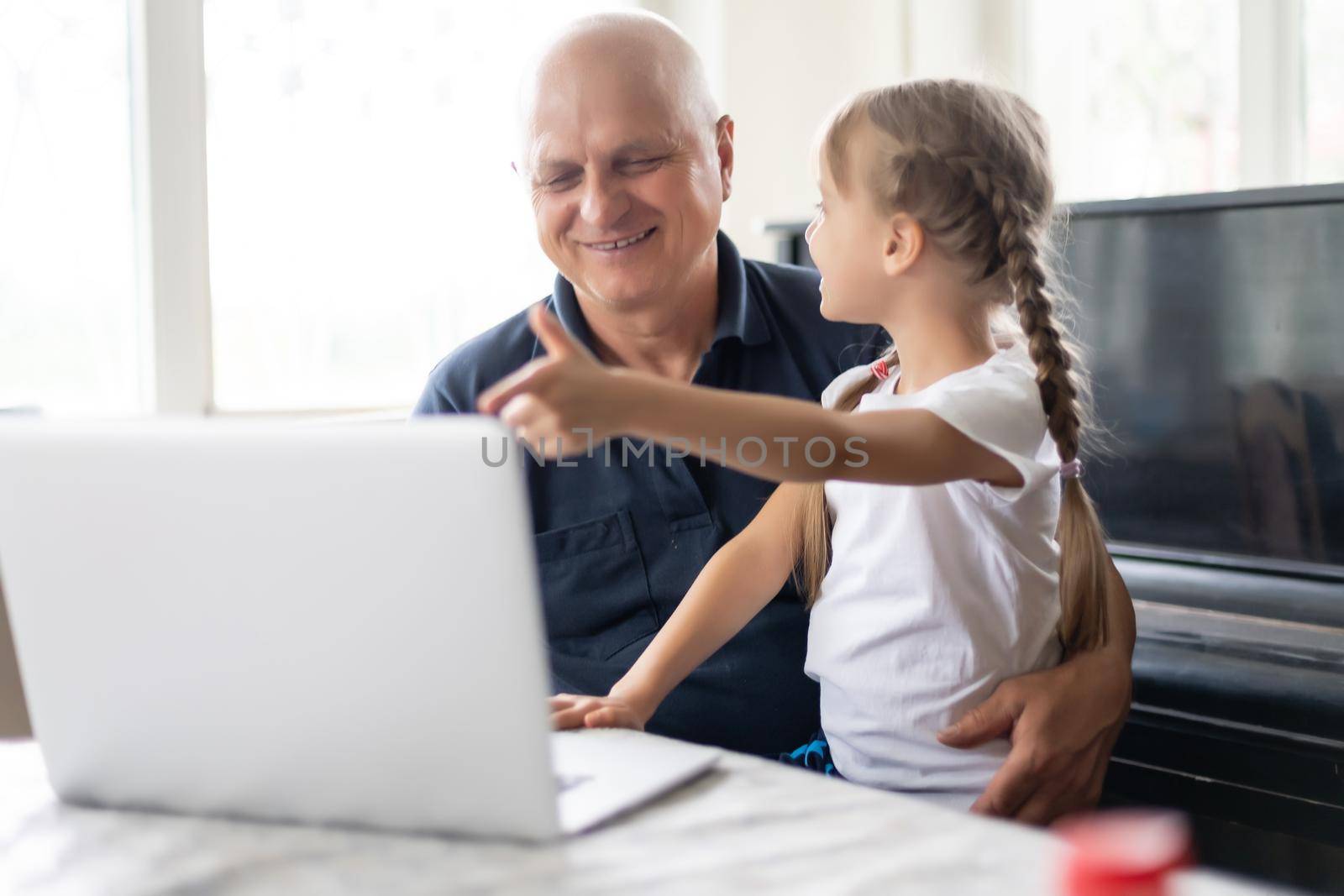 Portrait of grandfather and granddaughter doing homework with laptop.