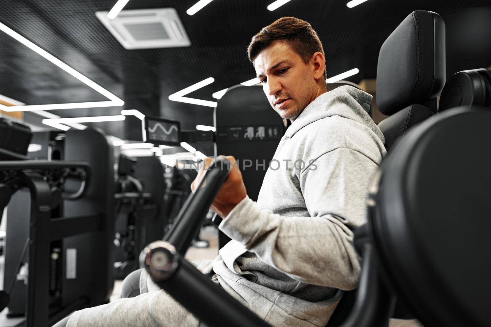 Young fit bodybuilder man doing arms workout training in the gym on machine, close up