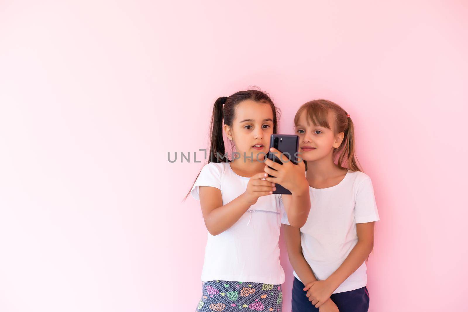 Two little girls playing with smartphones on a pink background by Andelov13