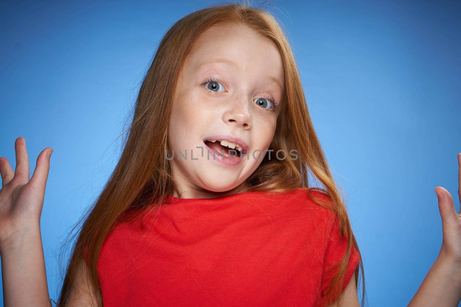 cute red-haired girl in red t-shirt emotions blue background. High quality photo