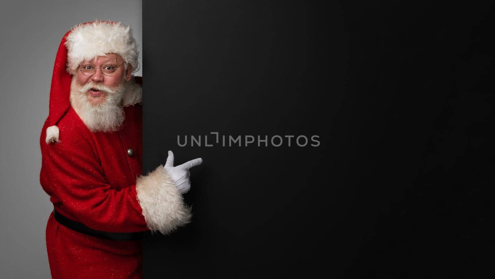 Santa Claus pointing at black paper billboard with copy space for text