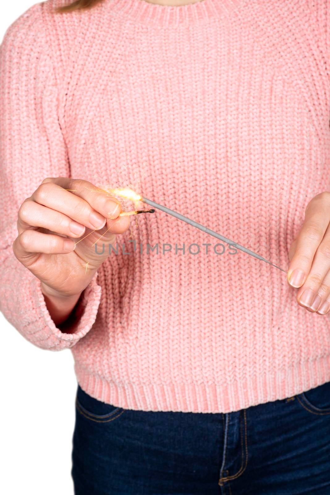 Close up of woman hands holding sparkler. Happy New Year concept. Girl in a pink knitted sweater sets fire to sparkler isolated on white