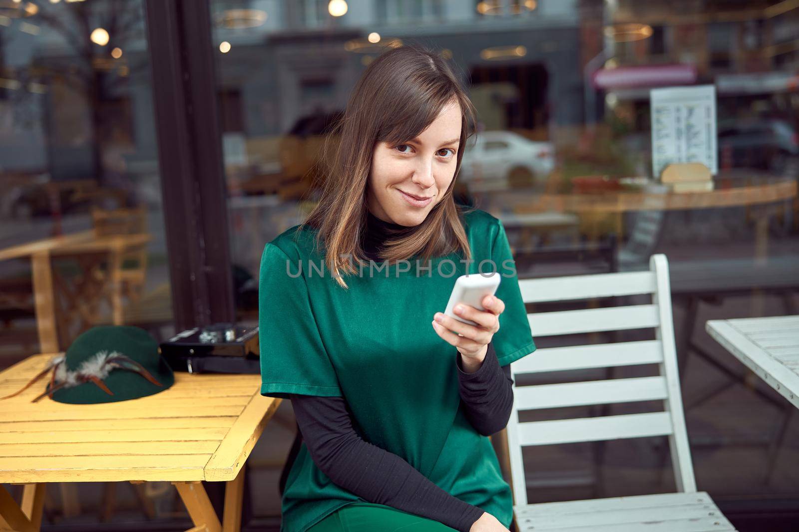 Portrait of cheerful young caucasian woman in green clothes that sitting outside cafe