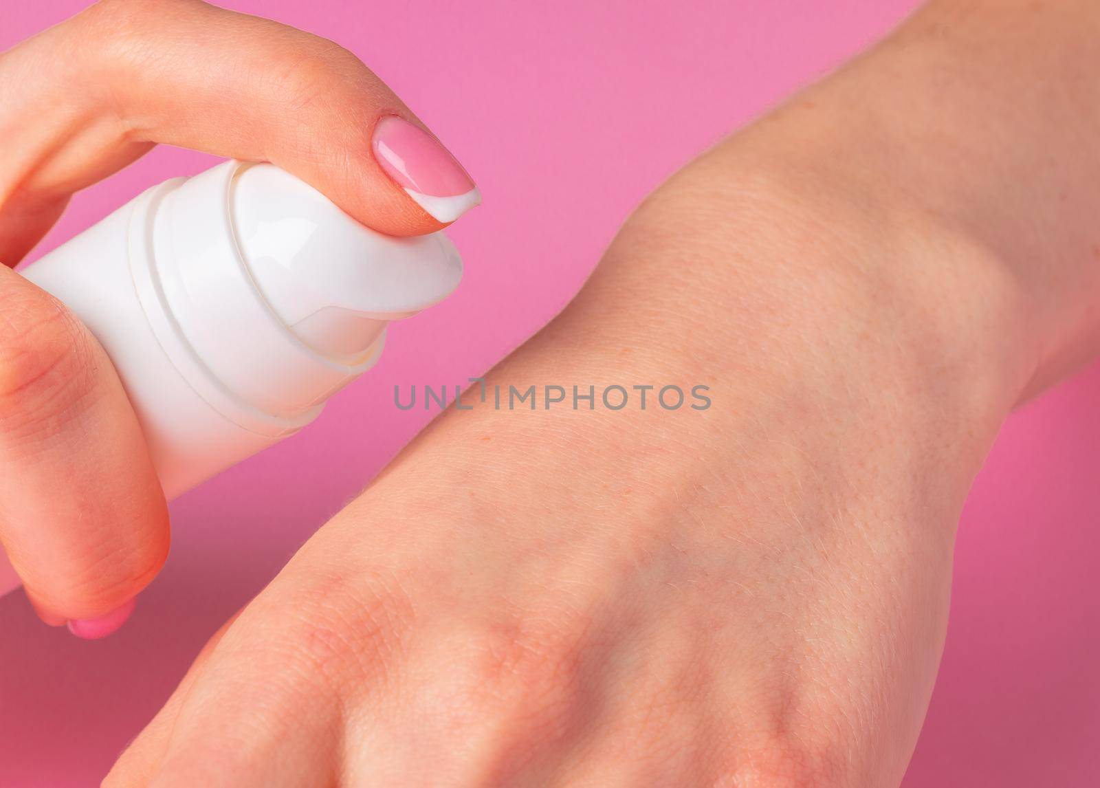 Female hand holding skincare product bottle on pink background