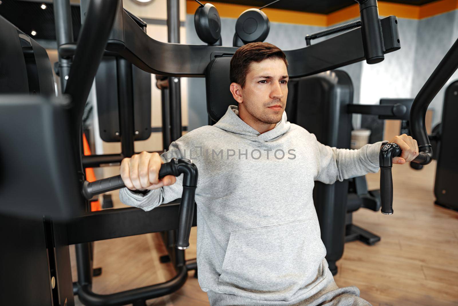 Young fit bodybuilder man doing arms workout training in the gym on machine, close up