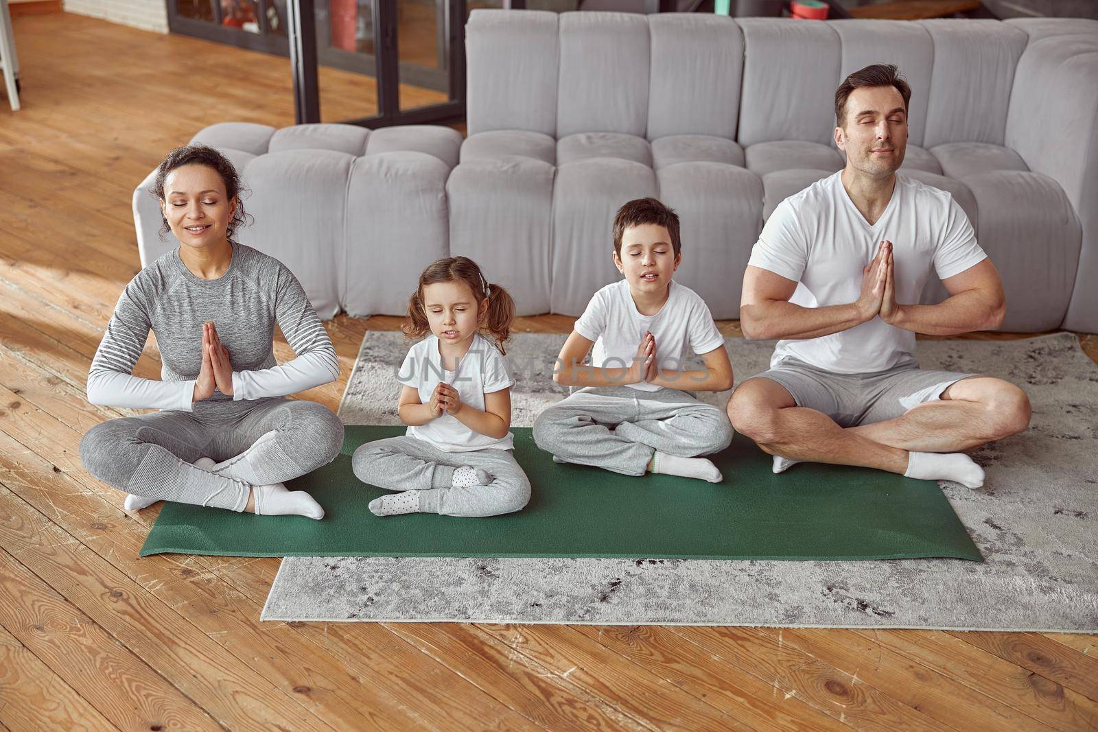 Top view of joyful parents with daughter and son sitting on floor in lotus position and doing meditation