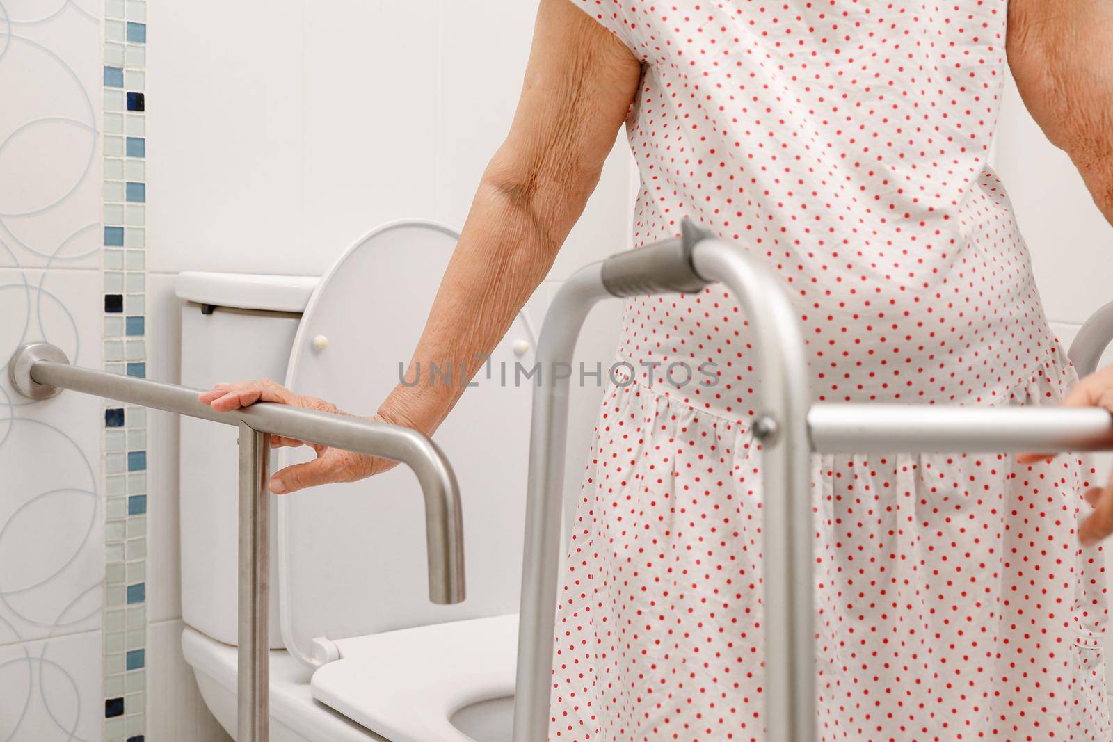 Elderly woman holding on handrail in toilet.